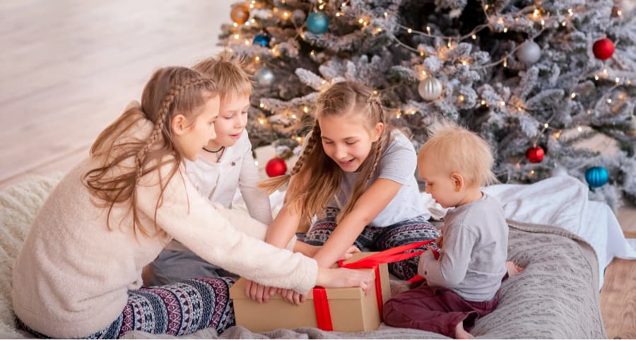 Kids opening a present next to a Christmas tree.